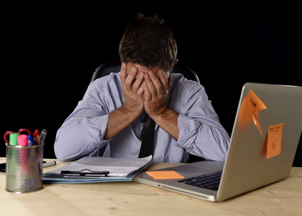 A frustrated professional with his head in his hands at a laptop
